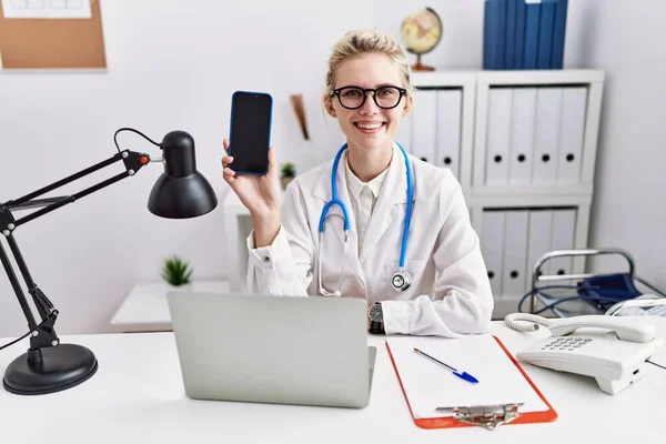 Young Doctor Woman Holding Smartphone Showing Blank Screen Looking Positive — Stock Photo, Image