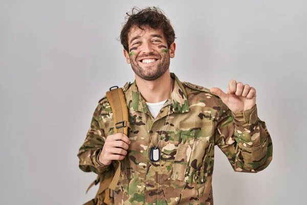 ヒスパニック系の若い男が手と親指で後ろを指してカモフラージュ軍の制服を着て 自信を笑顔 — ストック写真