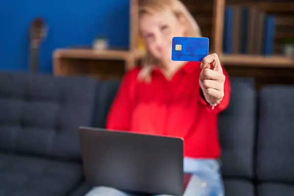年轻的金发女人坐在家里的沙发上 用笔记本电脑和信用卡 — 图库照片