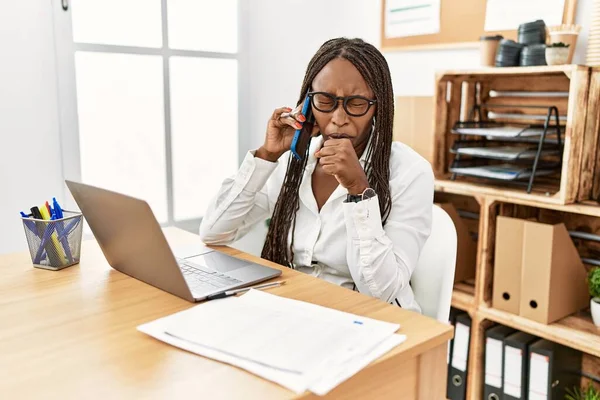 Black woman with braids working at the office speaking on the phone feeling unwell and coughing as symptom for cold or bronchitis. health care concept.