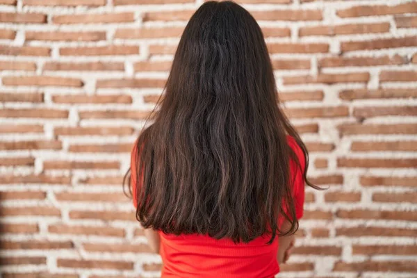 Young teenager girl standing over bricks wall standing backwards looking away with crossed arms 