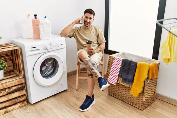 Young Hispanic Man Waiting Washing Machine Speaking Phone Laundry Room — 图库照片