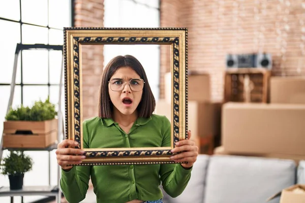 Young Hispanic Woman New Home Holding Empty Frame Shock Face — Stock Photo, Image