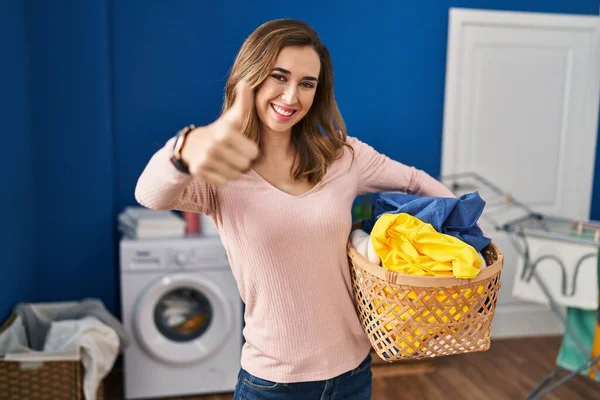 手で積極的なジェスチャーを行うことを承認洗濯バスケットを保持する若い女性 親指アップ笑顔と成功のために幸せ 勝者のジェスチャー — ストック写真