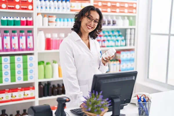 Young Beautiful Hispanic Woman Pharmacist Using Computer Holding Pills Bottle — Zdjęcie stockowe