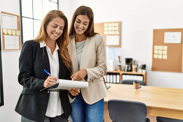 Mother and daughter business workers smiling confident reading document at office