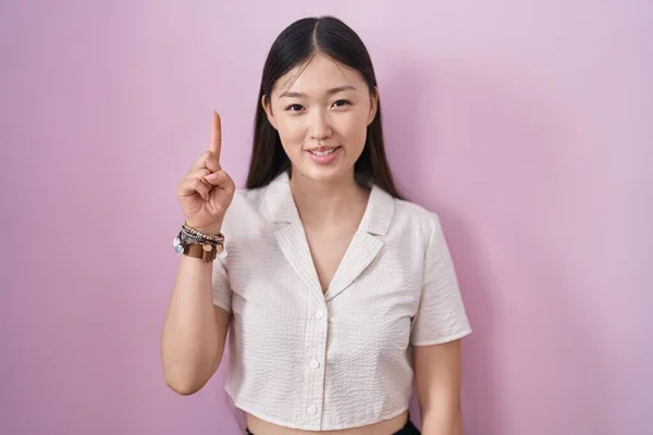 中国年轻女子站在粉红的背景上 带着第一指尖 自信而快乐地微笑着 — 图库照片