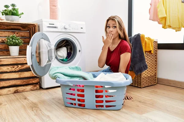 若い白人女性は手で口を覆う洗濯機に汚れた洗濯機を入れてショックを受け 間違いを恐れています 驚きの表情 — ストック写真