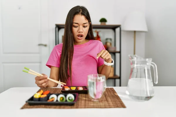 年轻的黑发女人用筷子吃寿司 手指朝下 露出广告 惊讶的脸和张开的嘴 — 图库照片