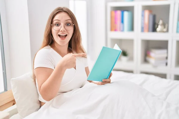 Mladá Běloška Sedí Doma Posteli Čte Knihu Usmívá Ukazuje Prstem — Stock fotografie