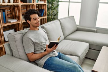 Evdeki kanepede oturmuş kitap okuyan genç bir İspanyol..