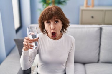 Orta yaşlı kadın bir bardak su içiyor. Korkmuş ve ağzı açık kalmış, şaşırmış ve şaşırmış. 