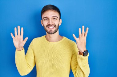 Mavi arka planda duran İspanyol adam dokuz numaralı parmaklarıyla gülümseyerek kendinden emin ve mutlu görünüyor.. 