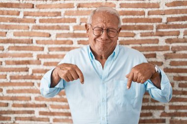Tuğla duvarın üzerinde duran yaşlı adam üzgün ve üzgün görünüyor, parmaklarıyla yönü gösteriyor, mutsuz ve depresif.. 