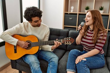 Genç çift klasik gitar çalıyor ve evde mikrofon kullanarak şarkı söylüyor..
