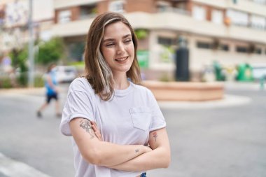 Kendine güvenen genç bir kadın caddede kollarını kavuşturmuş duruyor.