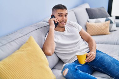 Genç İspanyol adam kahve içiyor ve evde akıllı telefondan konuşuyor.