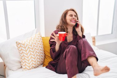 Genç, güzel, İspanyol bir kadın. Akıllı telefondan konuşuyor. Yatak odasında kahve içiyor.