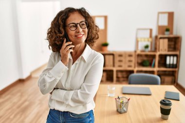 Orta yaşlı İspanyol kadın gülümsüyor ofisteki akıllı telefondan konuşuyor.
