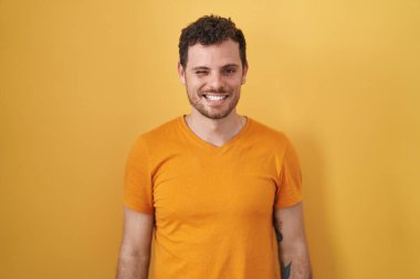 Sarı arka planda duran genç İspanyol adam kameraya seksi bir ifadeyle bakıyor, neşeli ve mutlu bir yüzle.. 