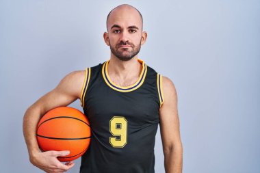 Basketbol forması giyen sakallı genç ve kel bir adam topu tutarken yüzünde ciddi bir ifade vardı. Basit ve doğal bir şekilde kameraya bakıyorsun.. 