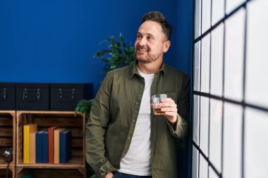 Genç beyaz adam evde dikilip bir bardak viski içiyor.