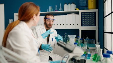 Laboratuvarda mikroskop kullanan kadın ve erkek bilim adamı üniforması giyiyor.