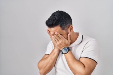 Beyaz arka plan üzerine günlük kıyafetler giyen sakallı genç İspanyol bir adam. Ağlarken yüzünü ellerle kapatan üzgün bir ifade. depresyon kavramı. 