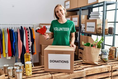 Gönüllü üniformalı beyaz bir kadın yardım merkezinde çalışan karton kutuları paketliyor.