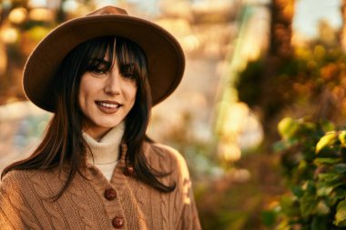 Parkta gülümseyen, kışlık şapkalı esmer kadın.