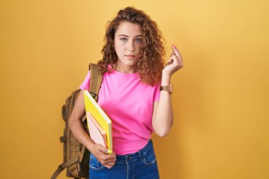 Genç beyaz kadın öğrenci çantası takıyor ve elinde kitaplarla İtalyanca jestler yapıyor. 