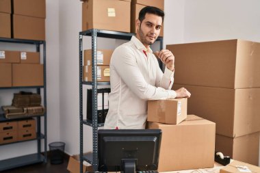 Ofisteki paketlere yaslanan Latin asıllı genç bir iş adamı.