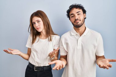 Gündelik giysiler giymiş genç bir çift kolları açık ve habersiz bir şekilde ayakta duruyor. Konseptten bihaber.. 