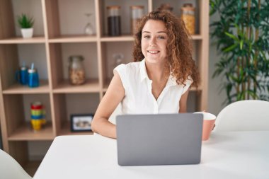 Genç ve güzel İspanyol kadın dizüstü bilgisayar kullanıyor. Evde kahve içiyor.