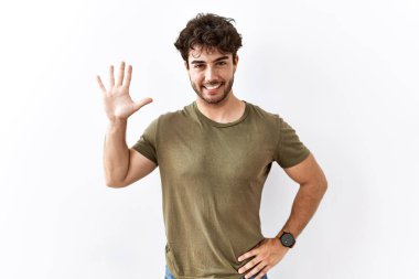 İzole edilmiş beyaz arka planda duran İspanyol adam beş numarayı gösterip işaret ederken kendinden emin ve mutlu gülümsüyor.. 