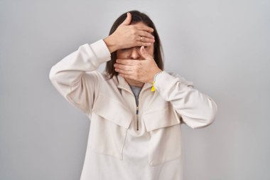 Orta yaşlı İspanyol kadın izole edilmiş arka planda duruyor. Gözlerini ve ağzını elleriyle kapatıyor. Şaşırmış ve şok olmuş. duygu gizleme 