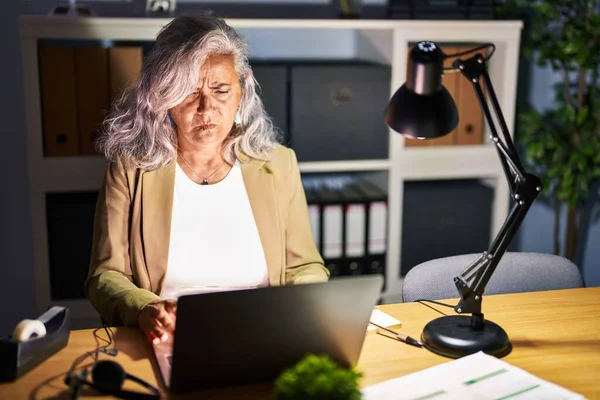 在深夜工作的中年妇女 头发灰白 在电脑笔记本电脑前工作时 疑神疑鬼 神经紧张 因为问题而皱着眉头 消极的人 — 图库照片