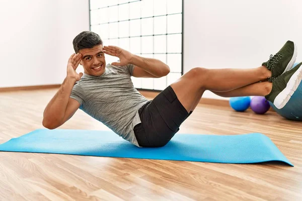 Genç İspanyol adam gülümsüyor spor merkezinde kendine güvenen karın kasları egzersizi yapıyor.