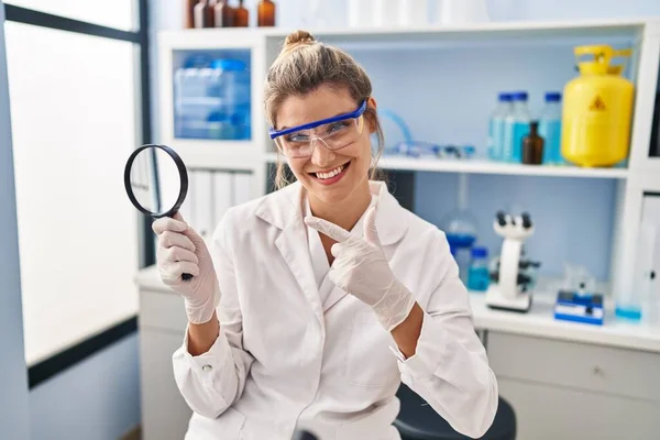 科学研究所で働く若い女性が手と指で笑顔を拡大鏡を持ちます — ストック写真