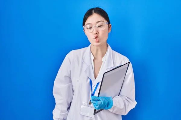 Chinese young woman working at scientist laboratory making fish face with lips, crazy and comical gesture. funny expression.