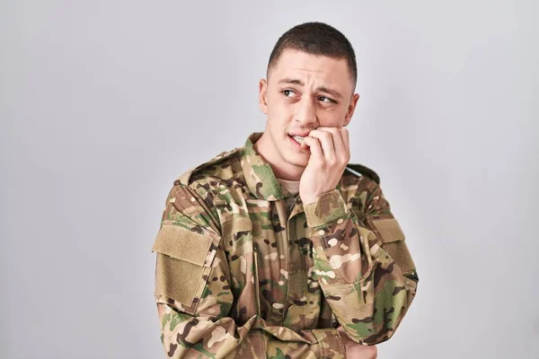 Young man wearing camouflage army uniform looking stressed and nervous with hands on mouth biting nails. anxiety problem.