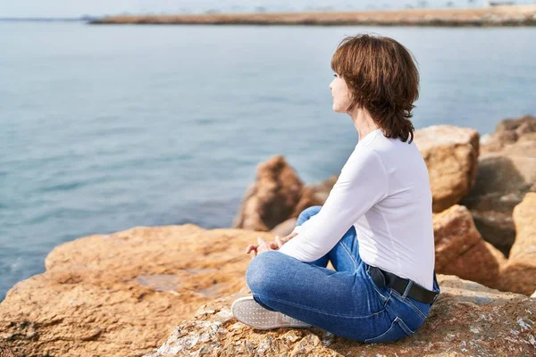 中年妇女自信地笑着坐在海滨的岩石上 — 图库照片