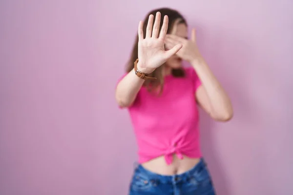 Blonde caucasian woman standing over pink background covering eyes with hands and doing stop gesture with sad and fear expression. embarrassed and negative concept.