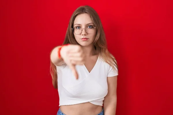Młoda Biała Kobieta Stojąca Nad Czerwonym Tłem Wyglądająca Nieszczęśliwą Wściekłą — Zdjęcie stockowe