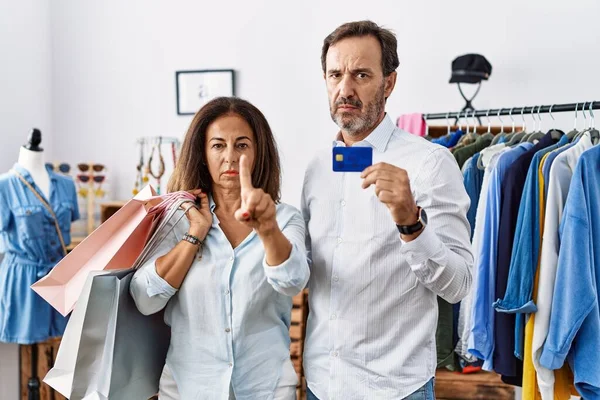 ヒスパニック系の中年カップルを保持ショッピングバッグとクレジットカード指摘とともに指アップと怒りの表情 いいえジェスチャーを示す — ストック写真