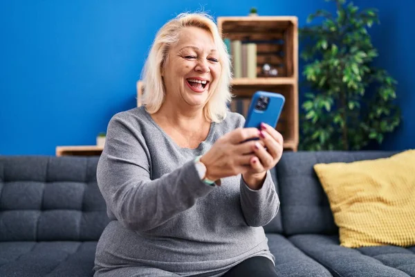 Blonde Frau Mittleren Alters Sitzt Mit Smartphone Hause Auf Sofa — Stockfoto