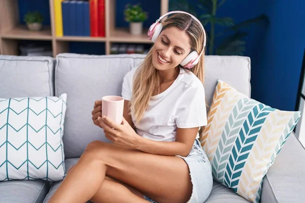 Genç sarışın kadın evde kahve içerek müzik dinliyor.