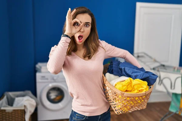 Ung Kvinna Håller Tvättkorg Gör Gest Chockad Med Förvånad Ansikte — Stockfoto