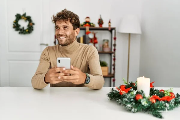 Νεαρός Ισπανόφωνος Άνδρας Χρησιμοποιώντας Smartphone Κάθεται Από Διακόσμηση Των Χριστουγέννων — Φωτογραφία Αρχείου