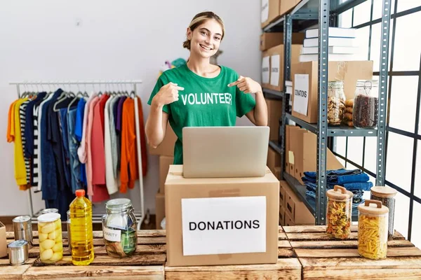 Bağışta gönüllü tişört giyen genç sarışın kadın yüzünde bir gülümsemeyle ayakta duruyor, kendini gururlu ve mutlu bir şekilde gösteriyor.. 